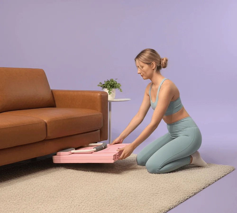 An image of a couch in a living room and the pilates board is folded in half and fitting under the couch.