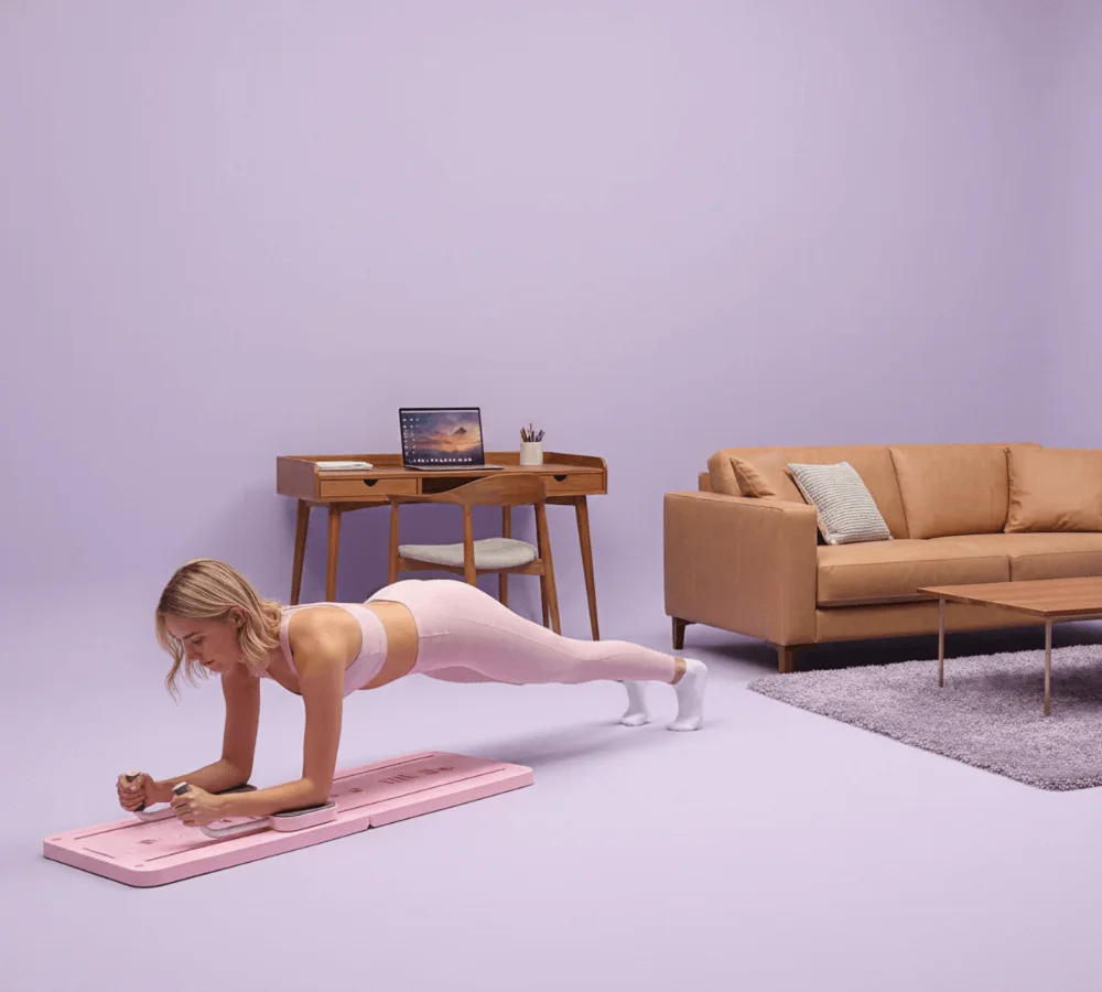 A woman in sportswear using a Pilates Reformer at home.